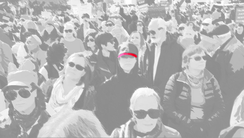 a black and white photo of a crowd at a 2017 Women's March. One hat is colored in pink